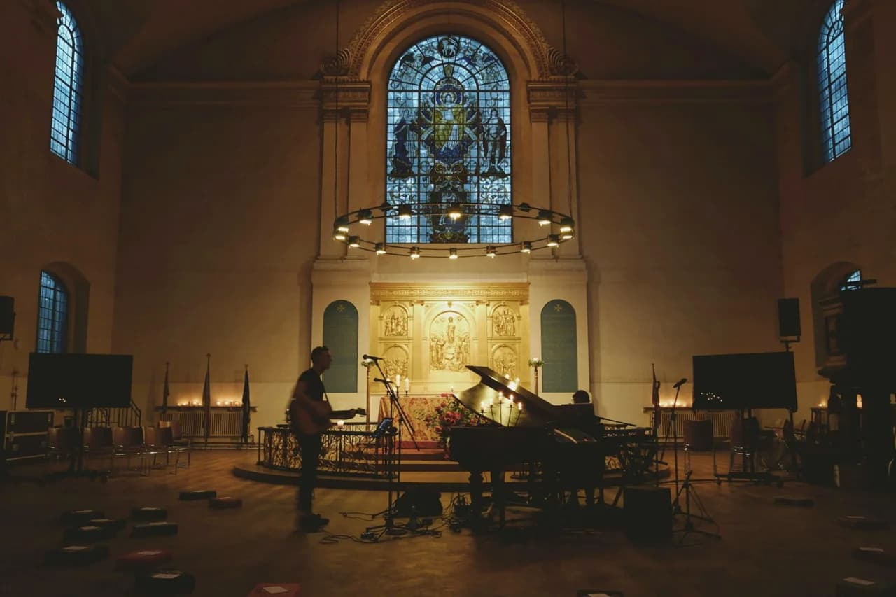 Des musiciens de sonorité[s] autour d’un piano à queue dans une église, devant un autel et un grand vitrail.