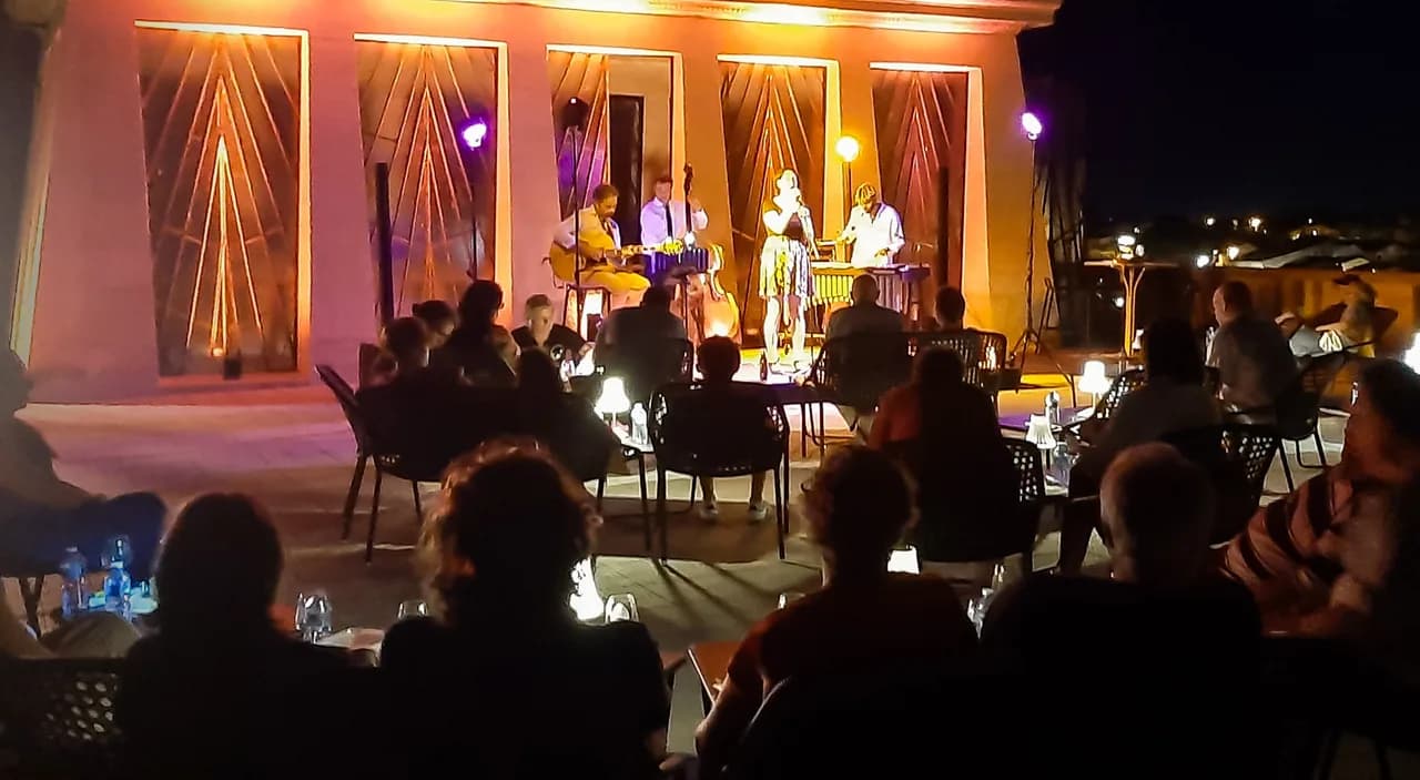 Une formation de sonorité[s] en concert de nuit sur une terrasse, devant un public attablé.