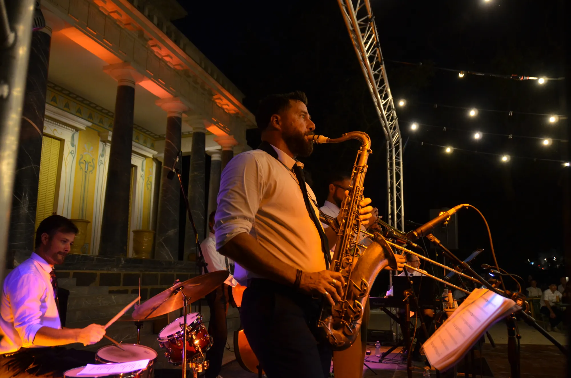 Un saxophoniste debout devant la batterie, sous la charpente lumineuse de la scène.