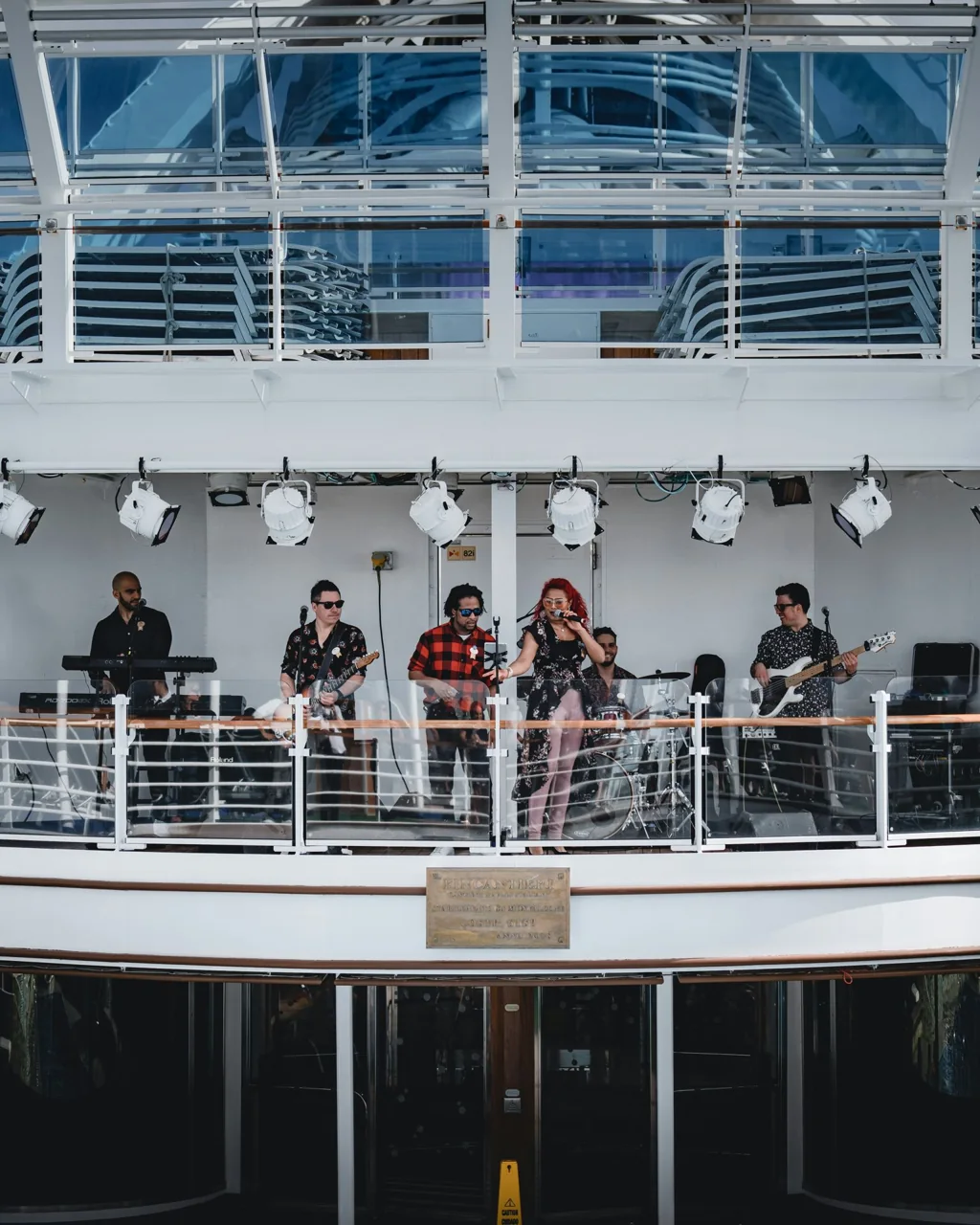 Des musiciens sur une terrasse en hauteur, sous une rangée de lampes.