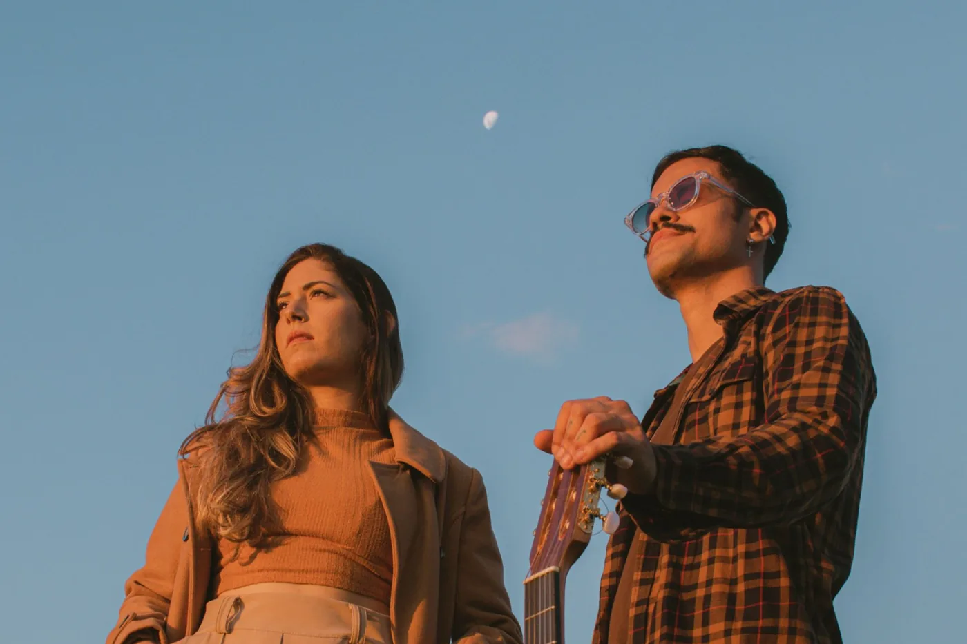 Un duo chant et guitare, debout sous un ciel de fin de journée