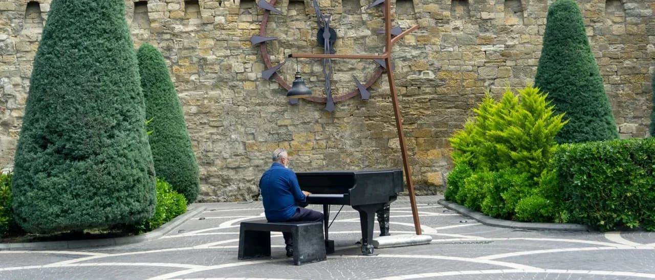 Un pianiste joue dans une cour pavée, entre les ifs taillés et un mur de pierre ancien