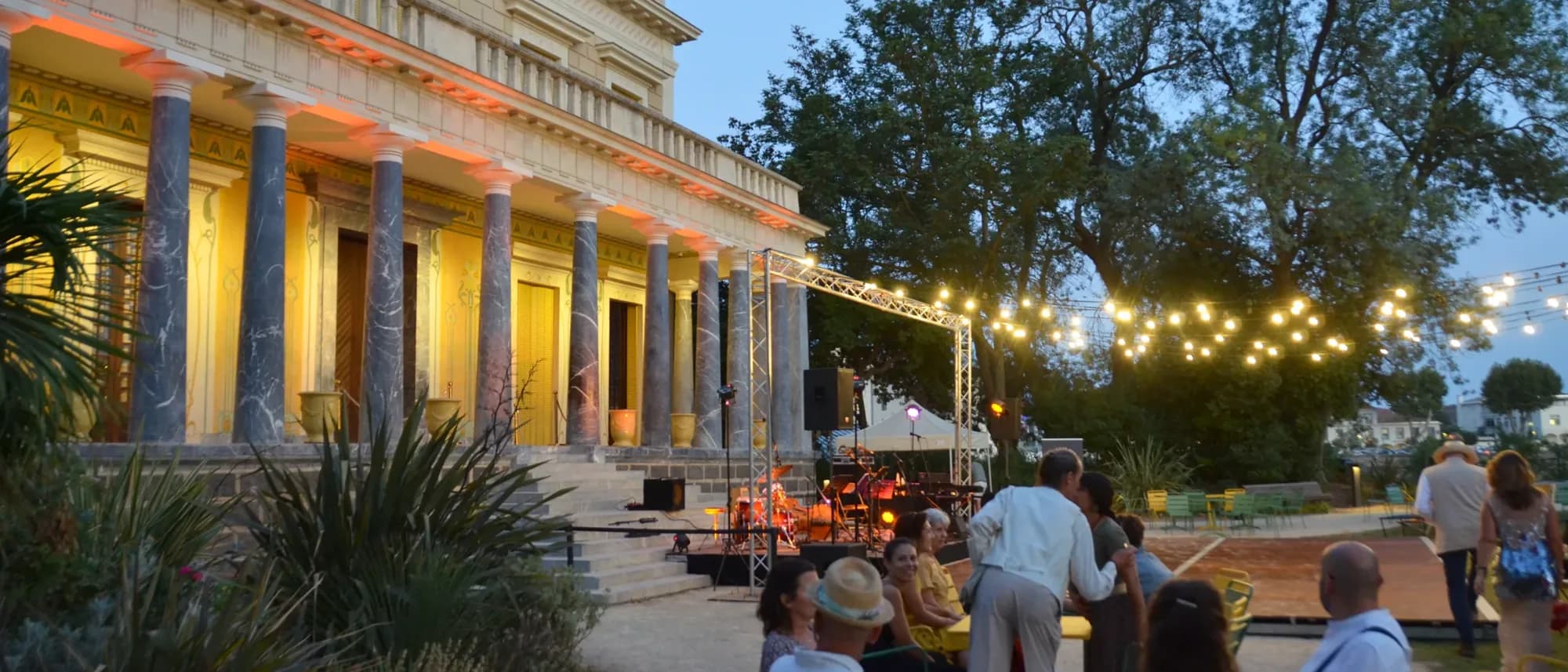 Le public attablé devant la scène, au pied de la façade illuminée du Château Laurens, à la tombée du jour